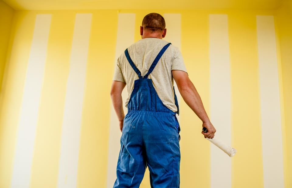 A painter working steadily across a wall with a roller