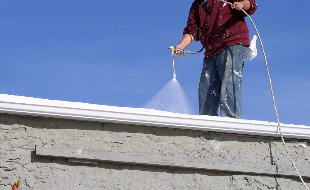 White elastomeric coating sprayed out along a stucco roof edge against a blue sky